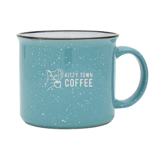 A teal ceramic mug with 'Kitty Town Coffee' logo engraved on it.